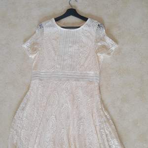 En cream färgad klänning som är ankel lång. Kortärmad. Består av två lager, det övre är spets. Under klänningen går till mitten av låret. Asymmetrisk kjol.