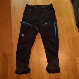 Revolution Race byxor - Ett par friluftsbyxor från Revolution Race, i modell Silence Pro. De är rätt så formpassade med stretch och en lite pösig passform (beroende på kroppsform skulle jag gissa). Supersköna att gå på promenader, vandringar eller svampplockning med. Inte isolerade eller något, men bekväma, med underställ under går de nog bra att ha dem även när det börjar bli kallt. Finns "vädringsfickor" på låren. De är hela och fina,förutom den vänstra översta fickan som har hål i. 