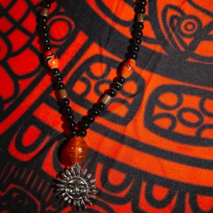 Halsband med solhänge - Handgjort (av mig) halsband med svarta pärlor, orangea glaspärlor, träpärlor samt ett solhänge i metall. Halsbandet är elastiskt och dras lätt över huvudet. 🌞💛