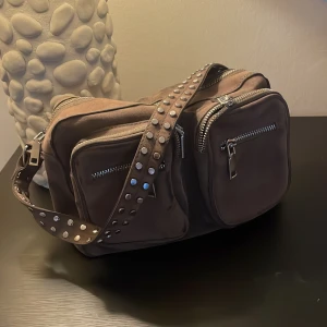 Noella axelremsväska  - Axelremsväska i färgen army från Noella som är inköpt 2019. Några slitage på väskan ( se bild) skickar gärna fler bilder om så önskas. 