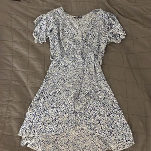 Klänning - Ljusblå sommarklänning med blåa blommor på. Köpt från SHEIN, sitter perfekt men anledningen till försäljningen är att den är för kort för mig (är 1.77cm). Tillkommer även ett band runt midjan i samma färg som klänningen. Knappast använd!