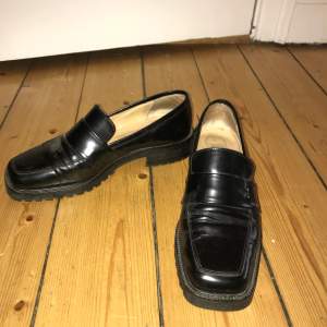 Svarta loafers blankt skinn storlek 37. Har haft metallspännen som plockats bort (se bild tre).
