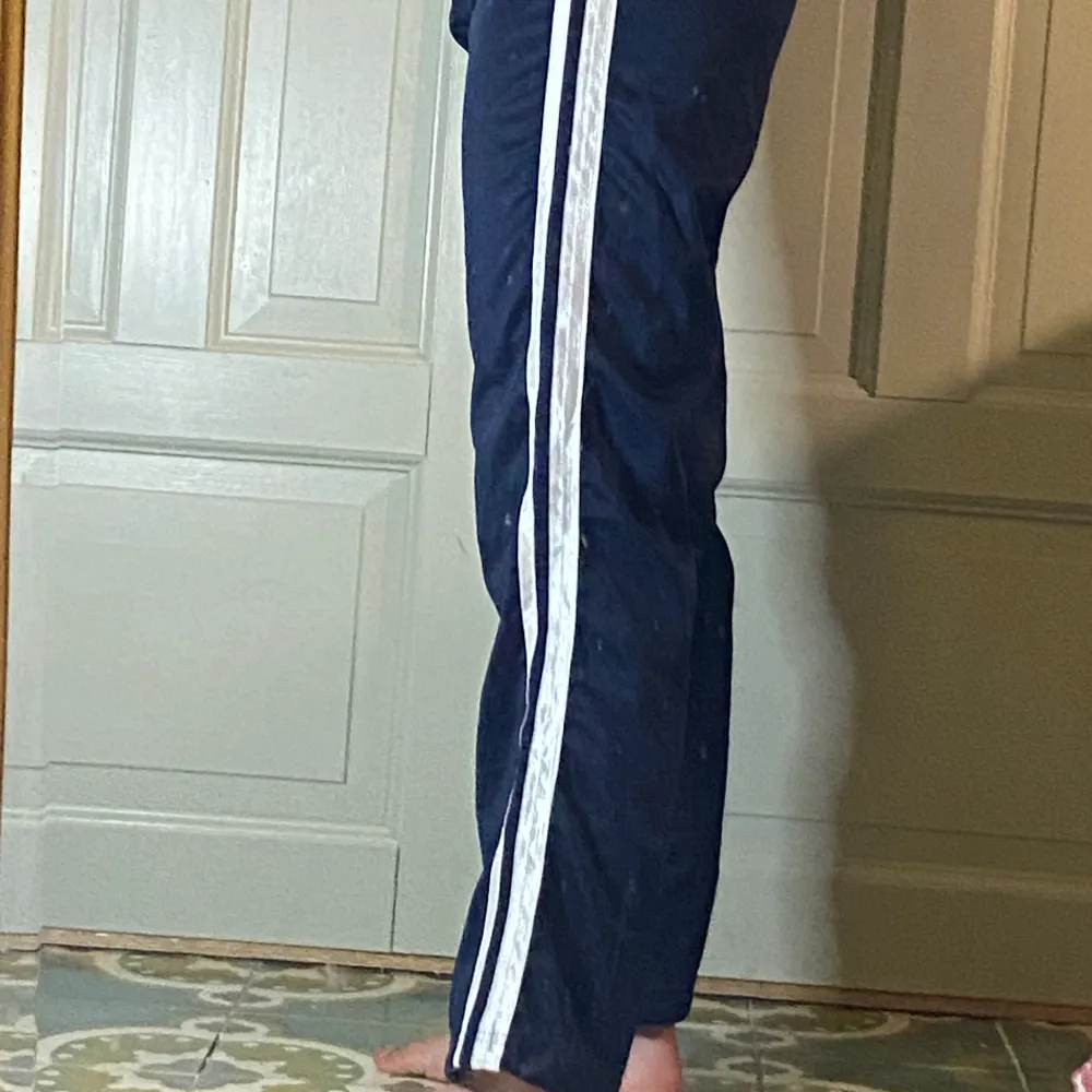 Mörkblå träningsbyxor från asics med vita ränder längs benen. Strlk S. Jeans & Byxor.