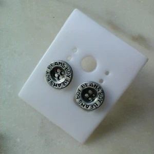 Örhängen - silverfärgade/mörka knappar i metall - Beams Boy - Örhängen som ser ut som knappar. Gjorda i någon typ av metall. Bara använda någon enstaka gång. Knapparna är ca 1 cm i diameter. Fraktpris 18 kr.