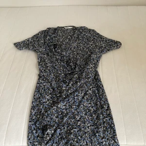Blommig klänning från Only  - Blommig klänning med mörkblå bakgrund, knytning i midjan. Sitter bra, storlek XS