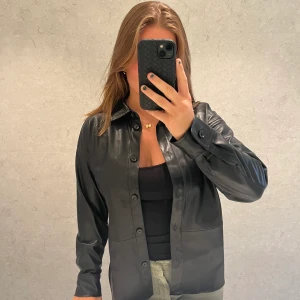 Skinnskjorta  - En supernajs skinnskjorta i lite oversized modell! Svarta detaljer. Hör av dug med eventuella frågor. Orginalpris 499kr😍 Nästan helt oanvänd och inga tecken på användning finns!!  Storlek S men passar även M💕