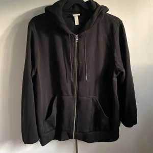 Svart zip-uphoodie/ munkjacka  - Det är en svart munkjacka i strl M, från HM. Den är som ny men andvänd några gånger. Den är super mysig och skön på insidan och passar perfekt som ett litet extra lager både inne och ute!  Köpare står för frakt, annars kan jag mötas upp i Kinna. 