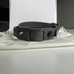 Balenciaga armband - Balenciaga armband i otroligt bra skick. Mörkgrå med svarta detaljer. Köpte det på Vestiaire men har aldrig använt det själv eftersom det inte passade mig.  Köparen står för frakten.