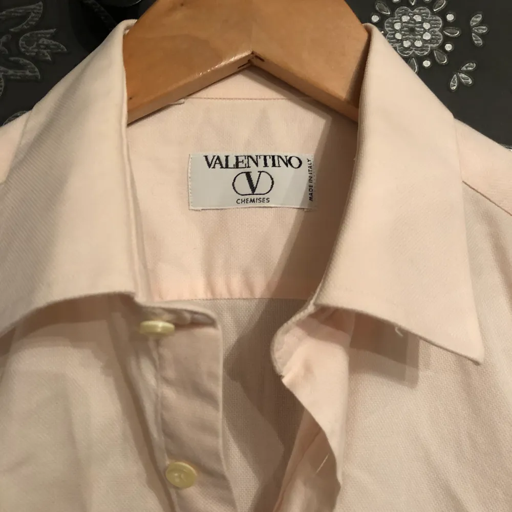 En Klassisk rosa Valentino skjorta i storlek 40 som motsvarar M. Den har även en fick vid vänstra delen av skjortan med det klassiska ”V”.  OBS som man ser i bilden så är skjortan ej struken vilket förklarar varför den är vrinklig annars är den i bra con, när man väl har strukt den. Skjortor.