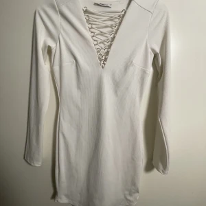 Klänning - Vit klänning. Lite festlig. Kurvsydd. Jag är 1,65 och öppningen får nästan till naveln. 