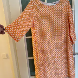 Kort klänning med något vid trekvartsärm. I mycket fint skick. Fodrad. Härligt orange-vitt mönster.