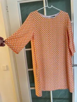 Kort klänning med något vid trekvartsärm. I mycket fint skick. Fodrad. Härligt orange-vitt mönster.