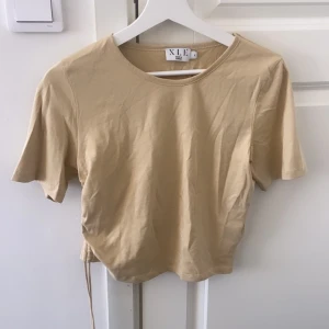 Topp - Cropad topp med detalj på sidan som man kan knyta.        Från Nakd Storlek S  Endast testad