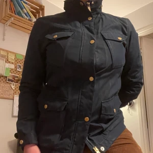 Peak Performance Jacka - Lite använd men fin marinblå höst/vårjacka med guldfärgade detaljer från Peak Performance. Skulle passa lite löst på XS-S (jag har storlek 38-40). Har en liten regn luva också som man zippa upp, plus 2 knappar vid handlederna så du kan välja hur tajt du vill ha det.