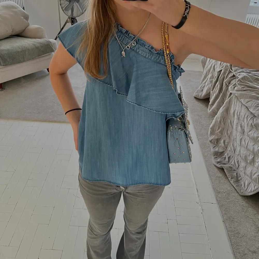 Skit snygg och cool jeans färgad blå blus/topp med volang över ens axeln. Helt ny och endast testad. Köpt på nk i Stockholm för 2 100kr (satte budgivning utifrån mitt senaste bud). Blusar.