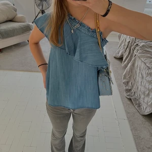 Mayla - Skit snygg och cool jeans färgad blå blus/topp med volang över ens axeln. Helt ny och endast testad. Köpt på nk i Stockholm för 2 100kr (satte budgivning utifrån mitt senaste bud)