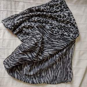 Lång grå/svart djurmönstrad sjal. Olika mönster på fram- och baksida. Nästan 2 m lång och 70 cm bred. Några dragna trådar. Tunn och lätt.