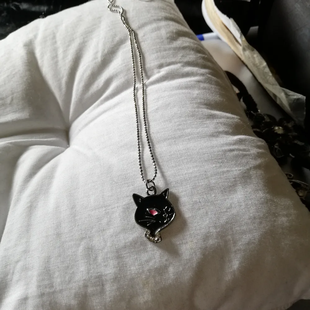 Ett halspand med ett svart katt huvud som har så sa öga och blinda med det andra samt ett lite kristalhalsband matrejal är metal . Accessoarer.