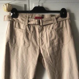 Lågmidjade beiga byxor - Jättefina lågmidjade byxor med en fin längd. Bakfickor fram vilket jag tycker är lite unikt. Innerbenslängd 81cm. Midja 85cm men det finns ju bälte som gör det diskret att dra åt till önskad storlek. 