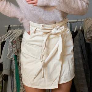 Asball kjol i omlott-modell i beiget jeanstyg. Kan bäras både med och utan skärpet. Storlek 34/36