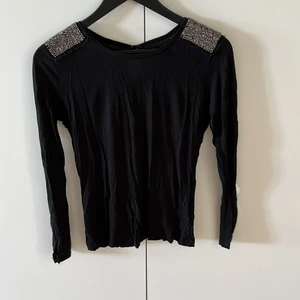 Svart tröja med detaljer på axlarna - Tunn svart träja i mjukt material. Silvriga pärlor på axlarna. Fint skick!