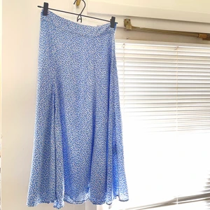 Blå blommig kjol - Blå kjol med vita små blommor och slits i sidan, perfekt sommarkjol! Säljer då den är för stor runt midjan. Jag är 166cm lång och den når ner till ungefär halva vaden på mig och slitsen går upp på halva låret.