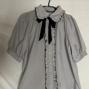 Blus Noemie - Grålila blus från det japanska märket Noemie! Blusen är luftig och kommer med ett band som kan knytas till en rosett runt kragen! Passar XS-S kanske liten medium! 