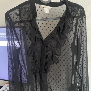 Stilren blus  - Blus i genomskinligt material med volang över bröstet 