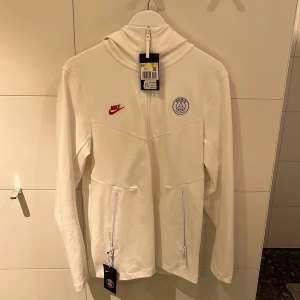 Nike tech zip hoodie - STEAL‼️Schysst vit Nike X PSG tech hoodie. Skick 10/10, helt ny aldrig använd bara testad. Alla tags är kvar. Storlek S men sitter som M (skulle även passa L). Nypris: runt 1200. 