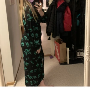 Långklänning grön/svart med slits  - En svart och grön långklänning med slits fram samt rynkning ovanför slitsen uppemot brösten. Smickrande passform. Dragkedja i ryggen