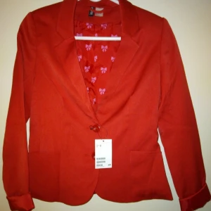 Helt NY & oanvänd kavaj. Röd. Storlek 36 / SMALL. - Helt NY och oanvänd klarröd kavaj. Storlek 36/SMALL. Material: Viskos, polyester. Stängs med knappar, har 2 små fickor och fint mönstrat satinfoder. Lappar/tags sitter kvar sedan inköpet. Inga defekter/fel.