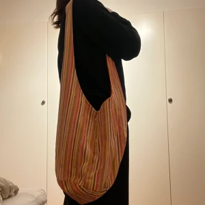 Randig tygväska - Jätte fin randig tygväska, jätte fin till stranden! Har ett hål på inner sida på bandet som syns på bild 3 (inget som syns när väskan är på). Djup 29 cm och bredd 33 cm. (Frakt ingår inte) 💚💗🧡💛