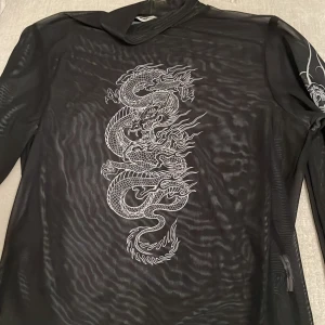 Mesh tröja - Svart mesh/genomskinlig tröja med text, rosor och en drake. Knappt använd, nästa nu.