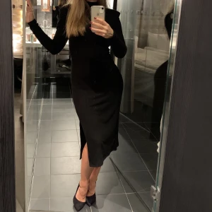 Svart ribbad klänning. Storlek S - Svart ribbstickad klänning med slits och axelvaddar. Använd endast en gång! 