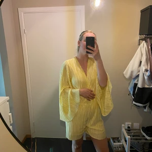 Gul playsuit  - Gul body från Nelly. Ett svalt och skönt material och stora trumpetärmar.