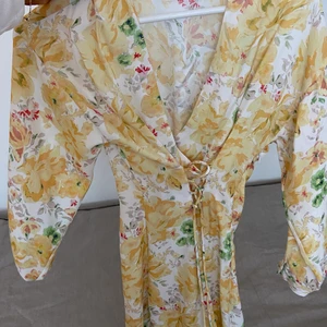 Klänning från Zara - Superfin kort klänning från Zara med blommönster och en liten korsett i midjan som spänner åt hur klänningen ska sitta. Dragkedja på sidan och knappar i ärmarna