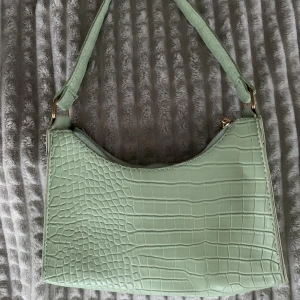 Grön axelremsväska  - Fin pastellgrön axelremsväska i crocomönster💚 Guldkedja och guldspännen med svart foder Använd fåtal gånger och inget slitage