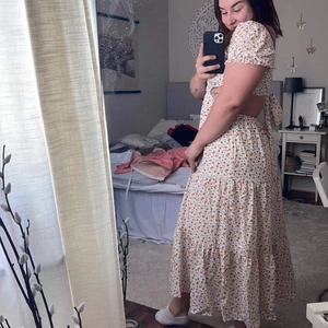 Kiss the Sky klänning  - En midsommardröm! Långklänning med blommigt mönster, öppen rygg, knytning bak, puffärmar och en vackert fallande maxikjol. Passformen är justerbar med knytningen i ryggen och ärmarna går att lägga som ’off-shoulder’.