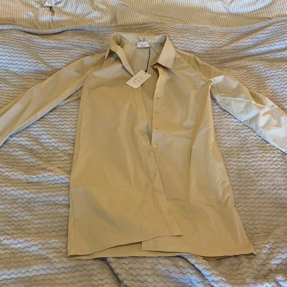 Säljer denna beiga skjortklänning från AFJ: S kollektion med NA-KD. Aldrig använd och prislappen är kvar. Storlek 36 . Klänningar.