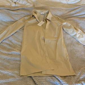 Säljer denna beiga skjortklänning från AFJ: S kollektion med NA-KD. Aldrig använd och prislappen är kvar. Storlek 36 