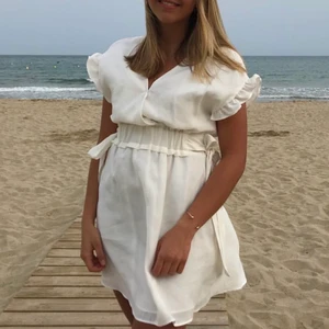 Vit klänning - Vit klänning från zara med fina justerbara rosetter på sidorna. Perfekt att ha som både kjol och klänning!🥰