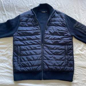 J Lindeberg Hybrid (cardigan) Jacket. Knappast använd men har legat i garderoben ett tag men är i bra skick, inga flaws eller liknande.  Storleken är medium, säljes för 999kr + porto