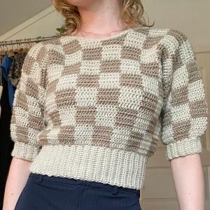 Virkad rutig beige/brun topp  - En egenvirkad topp i brunt och beige rutigt mönster med beige muddar. Skulle säga att den passar som en M (har själv stl 36/38 S/M).  Du som köper står för frakt om du vill ha levererat, möts annars upp vid Stockholm city. 