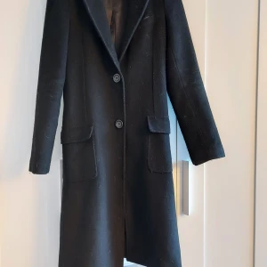 Svart ullkappa - Svart ullkappa från Wera Stockholm stl 34. Lite nopprig på vissa ställen men för övrigt i jätte fint skick. Innehåller 55% ull.  Kan ev bytas mot svart kappa stl 34/36 el s/m 