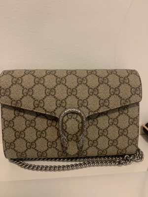 GUCCI dionysus gg supreme chain wallet - Väskan är helt ny och har ej kommit till användning, dustbag och äktbevis medföljs vid köp. Finns inga repor eller andra slags tecken på användning. Köpt på Farfetch. Väskan har mycket utrymme på insidan men är fortfarande liten och fin. 