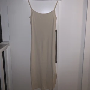 Tajt klänning - Tajt klänningen som är beige och har en slits på sidan av benet.