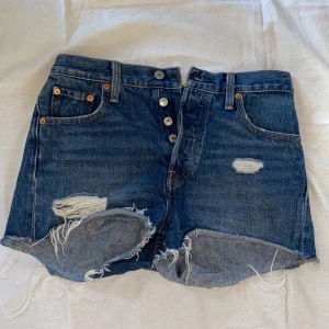 Jeansshorts - Ett par indigoblåa jeansshorts från Levis i modellen 501. Shortsen har lite fransar och hål samt knappar vid gylfen. Shortsen är i storlek W24. ✨🤍