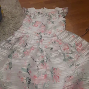 Barnkläning - Superduperfin barnklänning från London, perfekt för bröllop eller fest. Säljs då den adrig kommit till använding. Har fina blom motiv och ett bälte + en dragkedja på baksidan. 