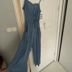 Jumpsuit &other stories, långa ben - Lugn blå jumpsuit från &other stories. Strl 40 men passar bra 36/38. Långa ben, tunna band upptill samt justerbart midjeband med knytning. Den är anväda kanske 5-10 ggr men är fortfarande i väldigt gott skick. Lite skrynklig nu pga legat i garderoben. 