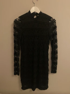 Spetsklänning - Svart klänning i spets. Långärmad med knäppning i nacken.  Köpare står för frakt 